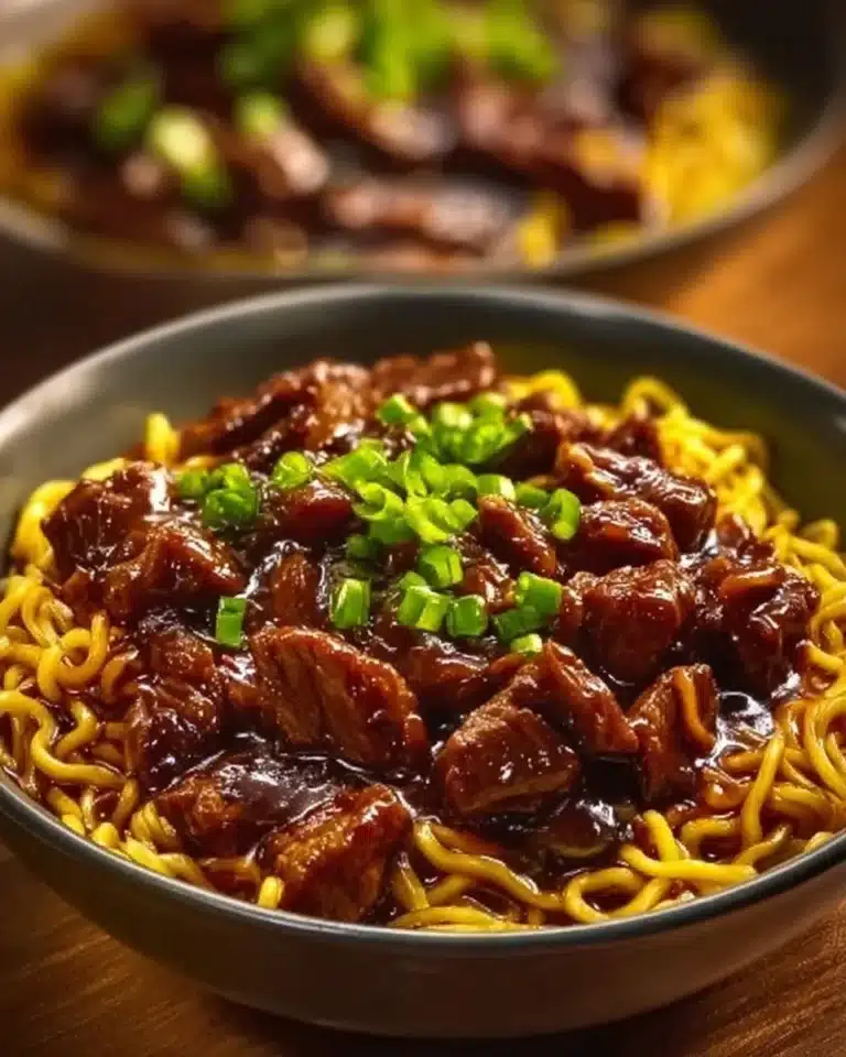 Plate of sticky beef noodles garnished with green onions and sesame seeds
