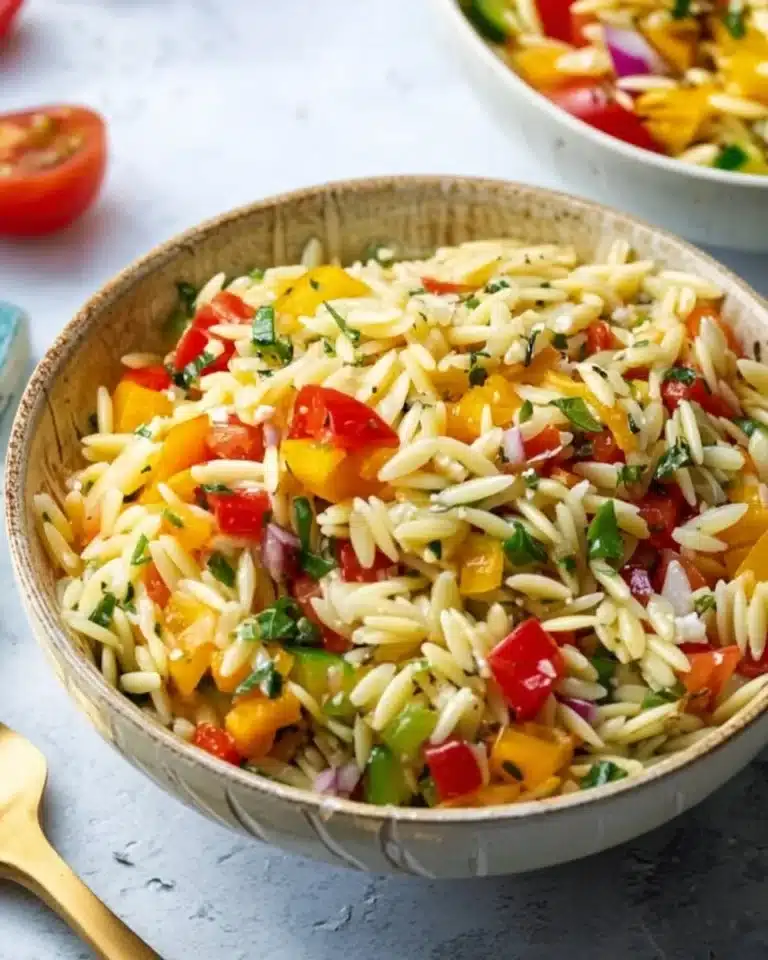 Colorful orzo salad with fresh vegetables and herbs on a serving plate.